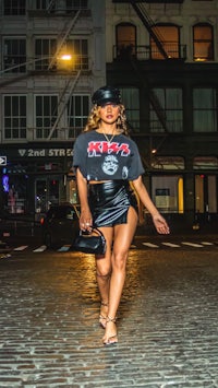 a woman in a leather skirt and hat walking down a cobblestone street