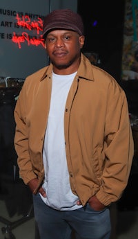 a man in a tan jacket standing in front of a neon sign